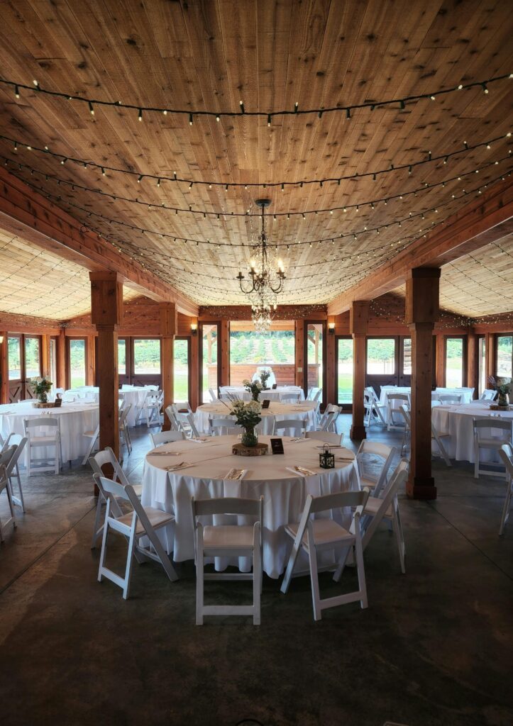 A beautifully lit rustic banquet hall with round tables and wooden ceiling, ideal for events.